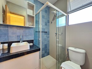 Un baño moderno con cabina de ducha de vidrio, un lavamanos con espejo y un inodoro.