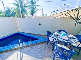Un área de piscina en la azotea con una piscina de azulejos azules, una mesa redonda con sillas y una sombrilla.