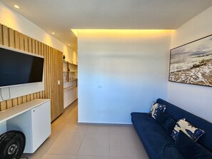 Ein modernes Wohnzimmer mit Fernseher, Sofa und einem Gemälde mit Strandmotiv.