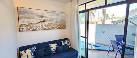 A modern living room with a blue sofa, a large abstract painting, and a glass door leading to an outdoor area with a pool and chairs.