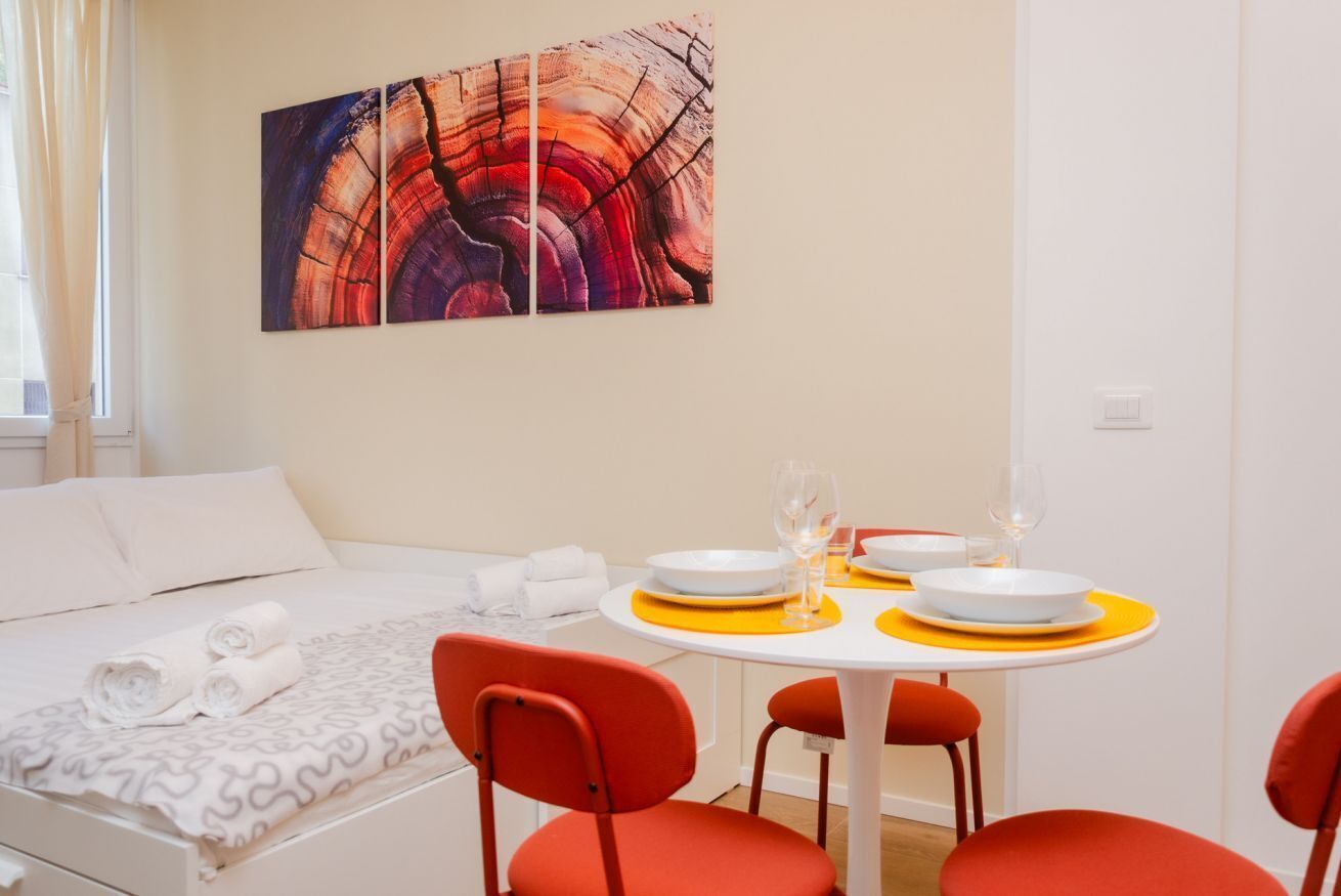 A hotel room with a neatly made bed, a dining table set with plates and glasses, and a large abstract painting on the wall.