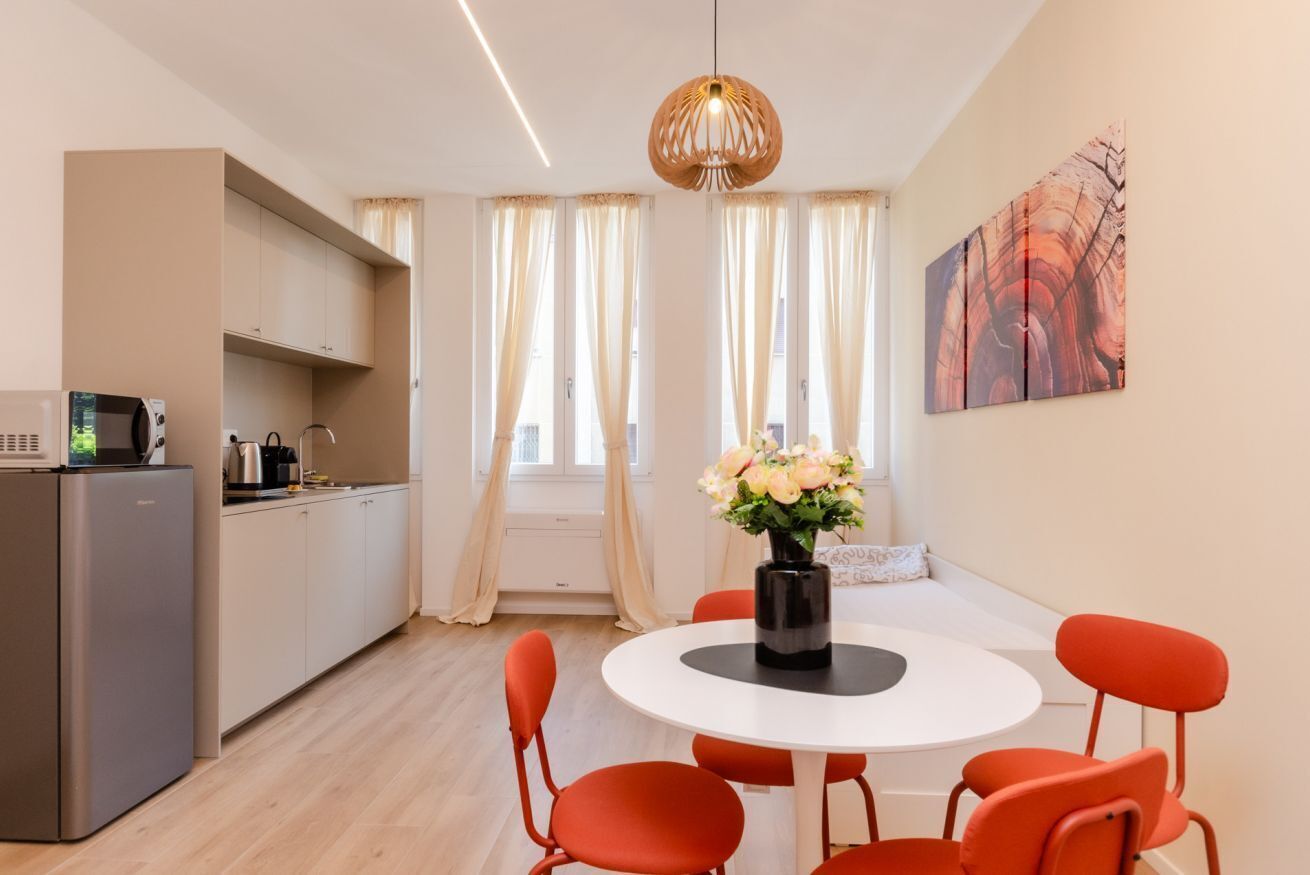 Eine moderne Küche mit Kühlschrank, Mikrowelle und Herd. Ein Essbereich mit rundem Tisch und orangefarbenen Stühlen.