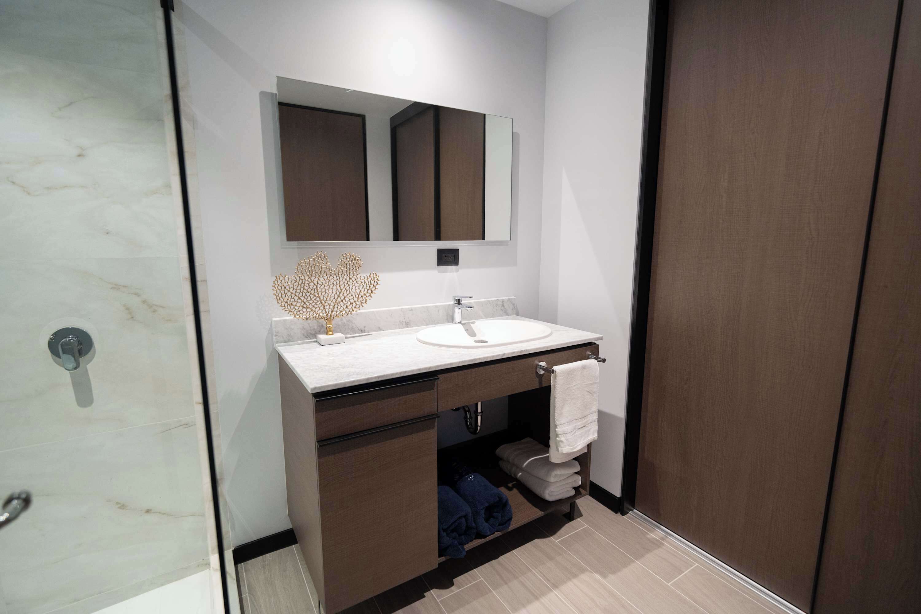 Uma casa de banho moderna com lavatório de mármore, um espelho grande e um porta-toalhas.
