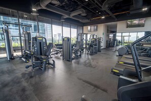 A modern gym with various exercise machines, treadmills, and a large window offering a city view.