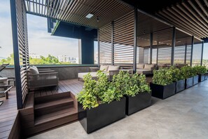 A rooftop terrace with wooden flooring, built-in planters with greenery, and outdoor seating.