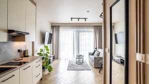 A modern kitchen with a built-in stove, a dining area with a round table, and a living room with a sofa and TV. - RentPlanet - Studio Zabrska (Katowice)