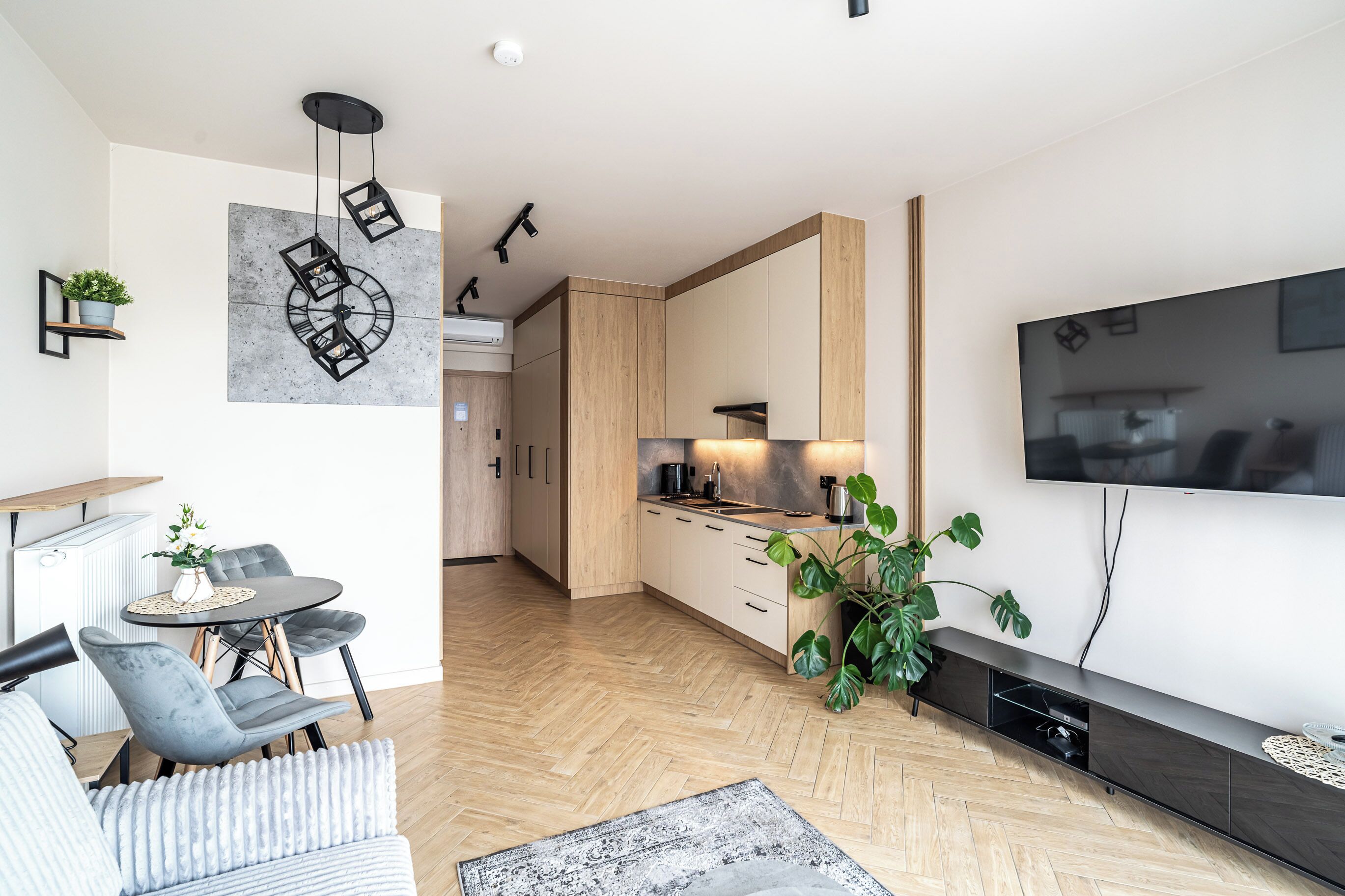 A modern living room with a flat-screen TV, a dining area with a table and chairs, and a kitchen with wooden cabinets.