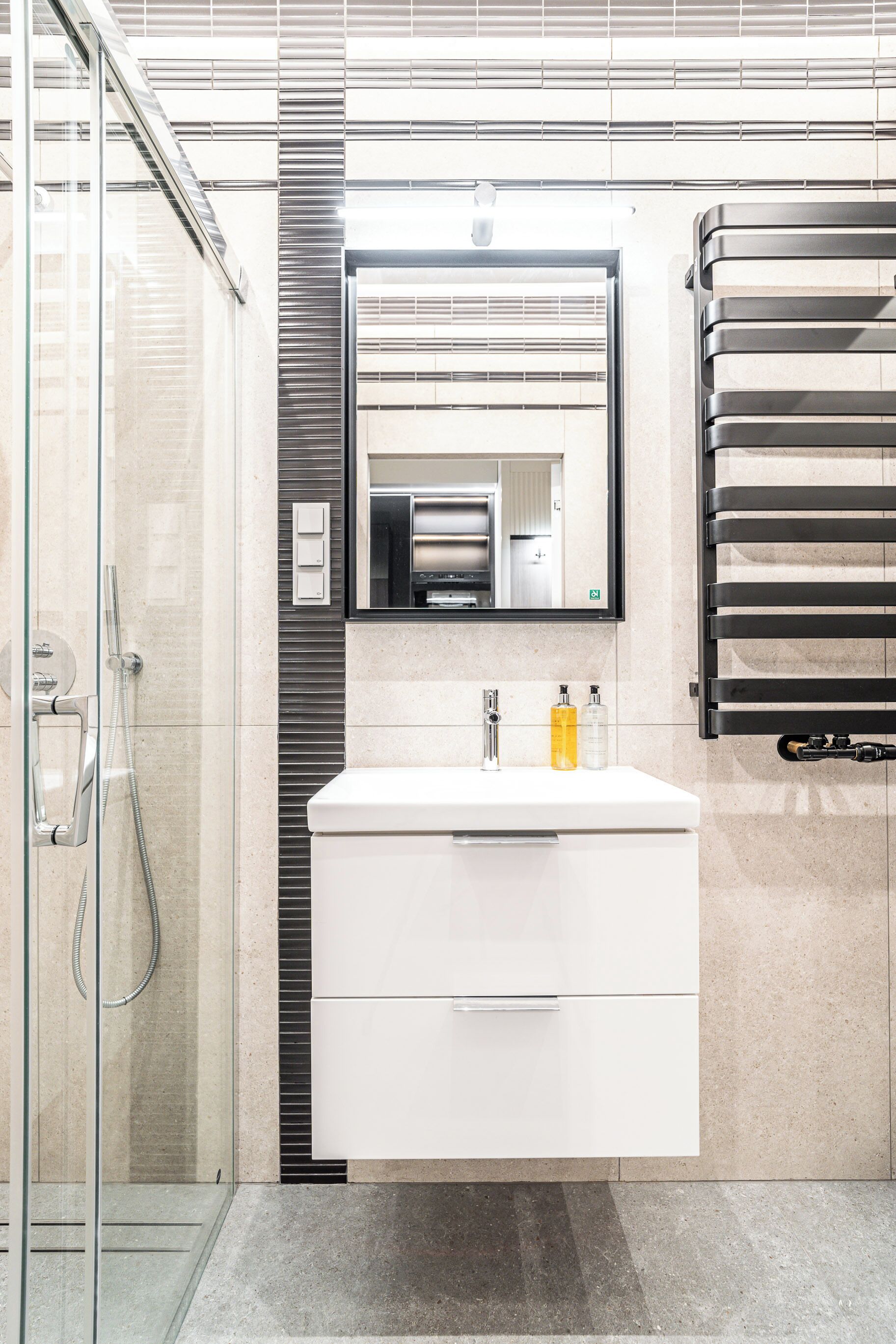 A modern bathroom with a glass shower enclosure, a white vanity with a mirror, and a black towel rack.