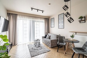 Un salon moderne avec un canapé, des fauteuils, un téléviseur et une grande fenêtre avec des rideaux.