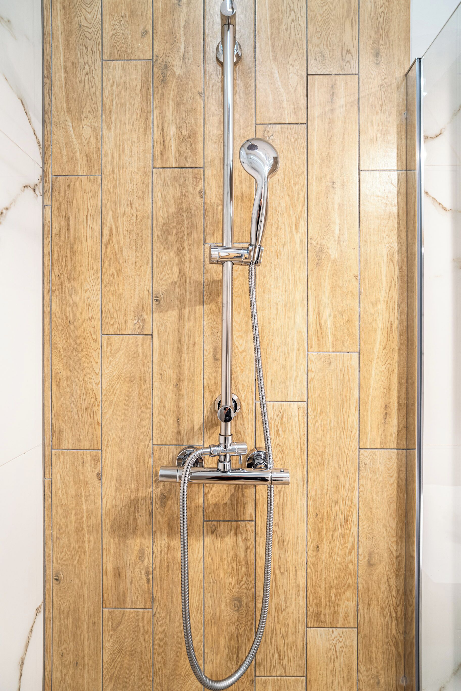 A shower with a chrome head and hose against a wooden wall.