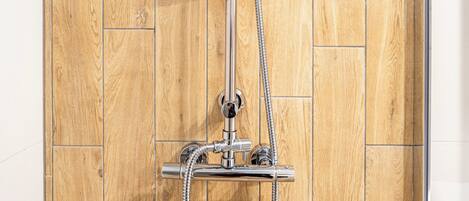 A shower with a chrome head and hose against a wooden wall.