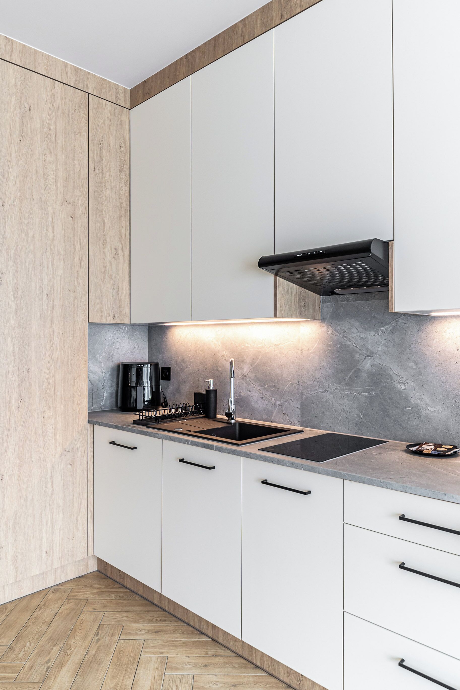 Una cocina moderna con armarios blancos, una campana extractora negra y un lavamanos de acero inoxidable.