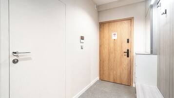 A hallway with a wooden door, a white wall, and a light-colored floor.