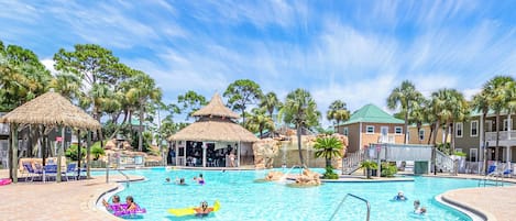 A swimming pool with palm trees and thatched-roof structures.