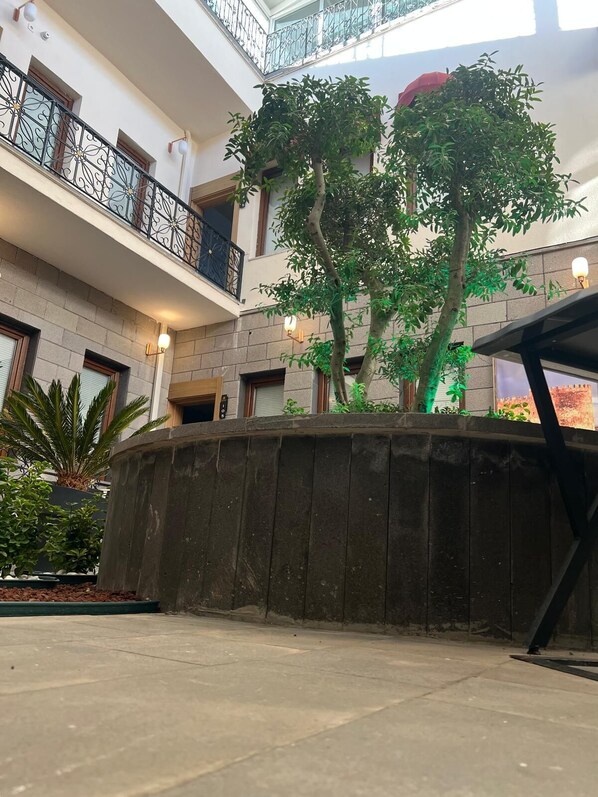 A multi-level atrium with a central garden area, stone walls, and a balcony with wrought iron railings. - Blackhan Palace Otel (Diyarbakır)