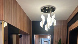 Un couloir moderne avec un lambris en bois, un miroir à cadre noir, un vase sphérique noir contenant des petits galets blancs et un luminaire au plafond.