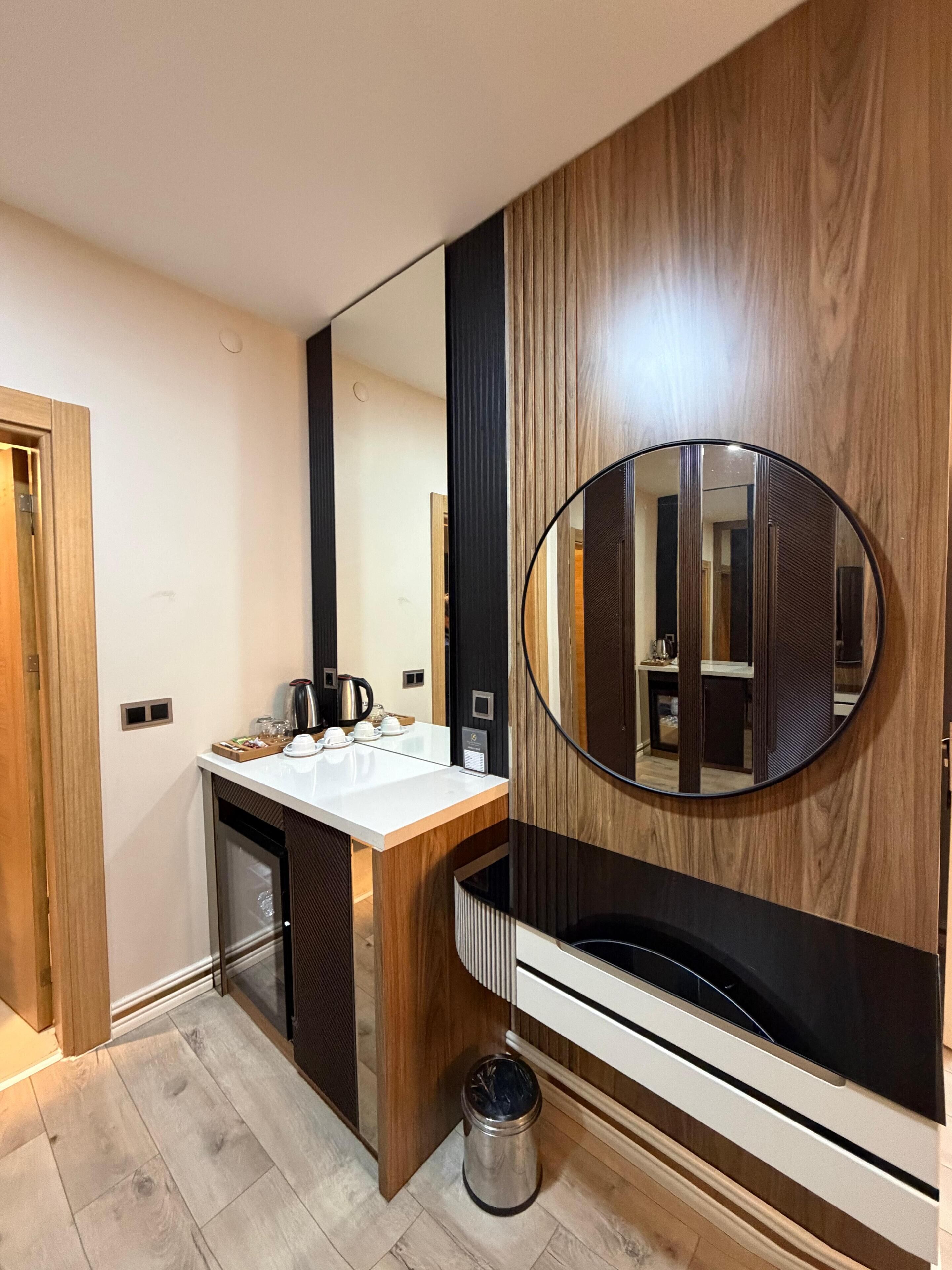 A modern bathroom with a wooden vanity, a round mirror, and a built-in heater.