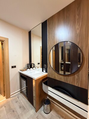A modern bathroom with a wooden vanity, a round mirror, and a built-in heater. - Blackhan Palace Otel (Diyarbakır)