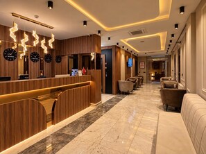 A hotel lobby with a reception desk, seating area, and a TV screen.