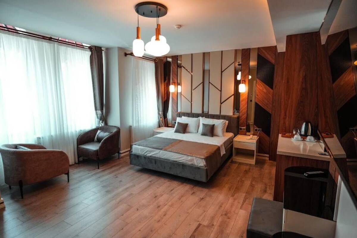 Ein modernes Hotelzimmer mit einem großen Bett, einer Sitzecke mit einem Sessel, einem Nachttisch und einem kleinen Schreibtisch mit Lampe.