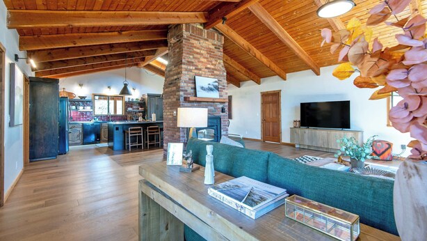 A spacious living area with a high ceiling, a brick fireplace, a television, and a cozy seating area. - Teton Homestead: Quaking Aspen Escape + Hot Tub (Driggs)
