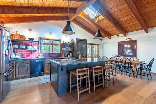 A spacious kitchen with wooden beams, a large island with stools, and a dining area with chairs. - Teton Homestead: Quaking Aspen Escape + Hot Tub (Driggs)