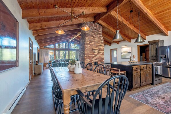 A spacious kitchen with a central island, wooden ceiling beams, and a large dining table with chairs. - Teton Homestead: Quaking Aspen Escape + Hot Tub (Driggs)