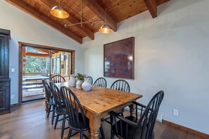 Un comedor con una mesa y sillas de madera, una araña y un cuadro en la pared.