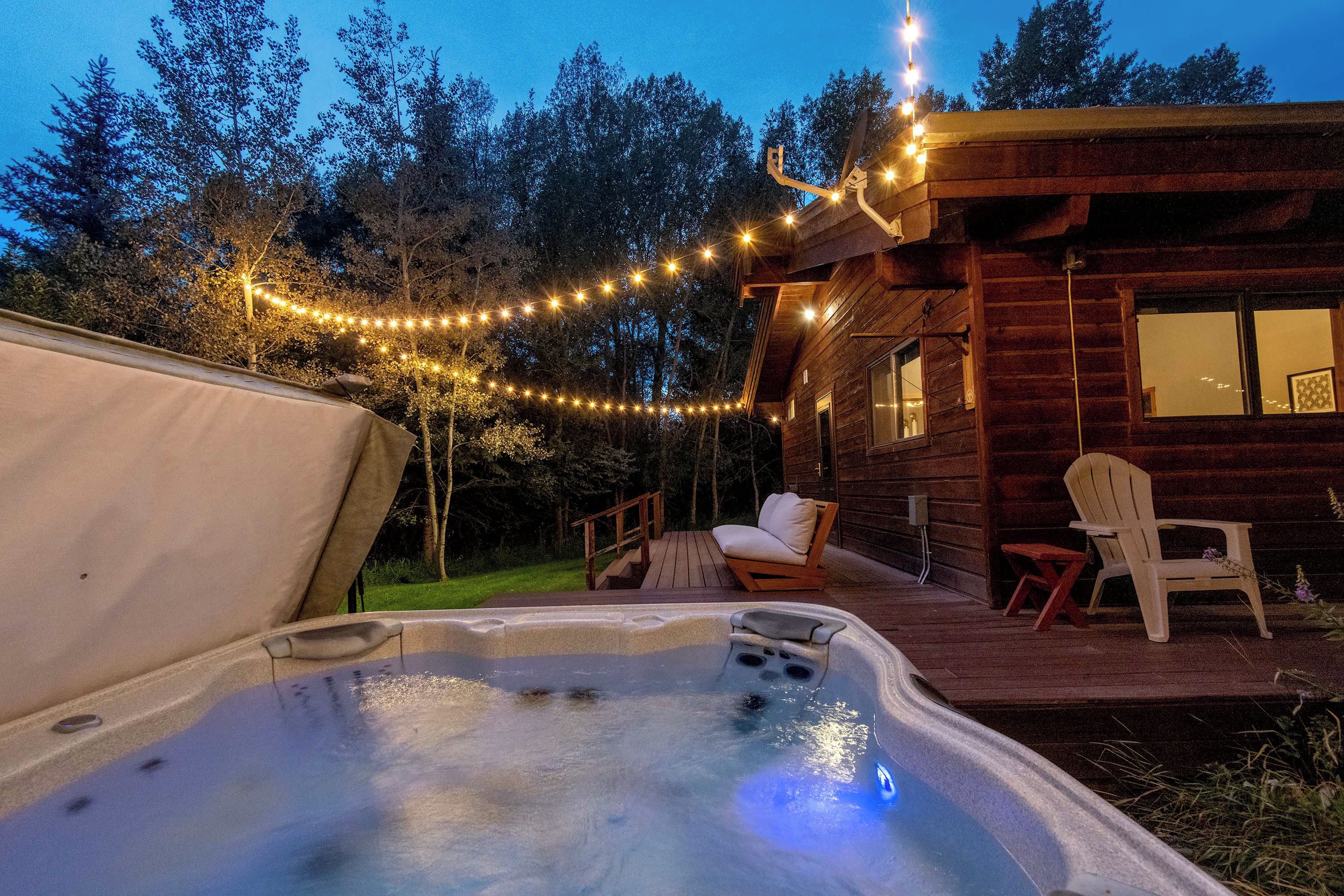 Puuinen mökki, jossa on poreallas, aurinkotuoleja ja koristeelliset valonauhat.