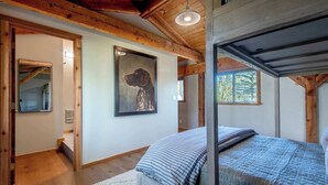 Een slaapkamer met een houten plafond, een ingelijst beeld aan de muur, een bed met een gestreept dekbed en een raam met uitzicht op bomen.