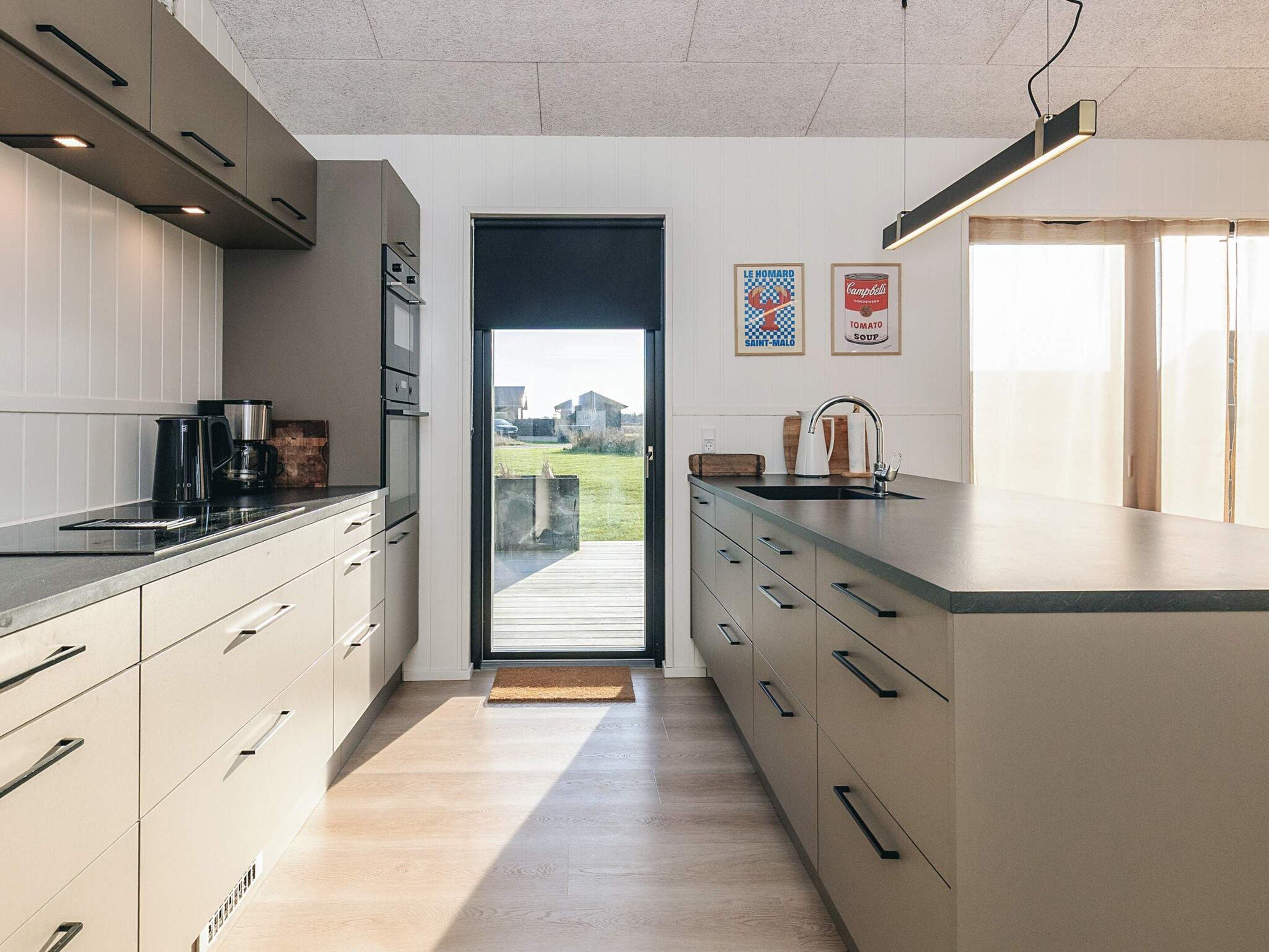 A modern kitchen with a large island, stainless steel appliances, and a view of the outdoors.