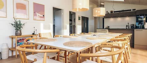 Un comedor amplio con sillas y mesas de madera, una cocina al fondo e iluminación colgante.
