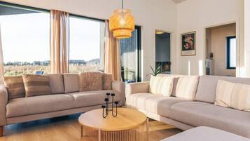 A modern living room with a large sectional sofa, a round wooden coffee table, and a hanging light fixture.