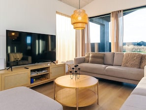 A modern living room with a flat-screen TV, a round wooden coffee table, a beige sofa, and a wicker lamp.