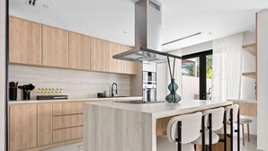 A modern kitchen with wooden cabinets, a central island with bar stools, and a large window providing natural light. - Arabian Ranches Villa Sleeps 9 Near Golf Courses (Dubai)