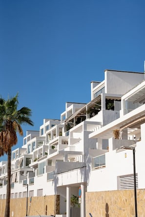 A modern multi-story building with balconies, white walls, and a clear blue sky.