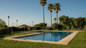A rectangular swimming pool with a tiled edge, surrounded by a well-maintained lawn and palm trees. - Stylish 2BR Apt | Balcony & Sea Views (Benalmádena)