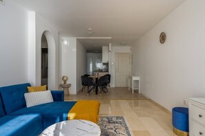 A living room with a blue sofa, a small round table, and a dining area with chairs.