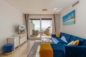A modern living room with a blue sofa, a small coffee table, and a TV on a white cabinet.