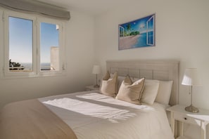 A bedroom with a bed, two bedside tables, a nightstand, a window, and a painting of a beach scene.