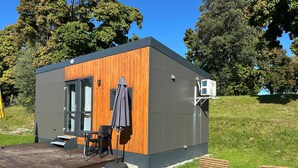 Une structure extérieure moderne avec une façade en bois, un patio doté de sièges et un appareil de climatisation.