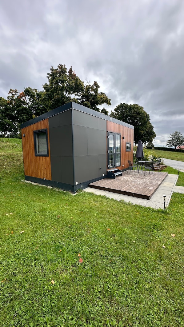 A modern, compact building with a wooden exterior, a glass door entrance, and a small outdoor seating area.