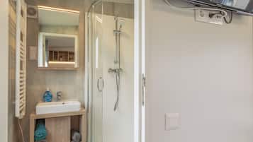 Ein modernes Badezimmer mit einer gläsernen Dusche, einem weißen Waschbecken und einem Spiegel darüber.