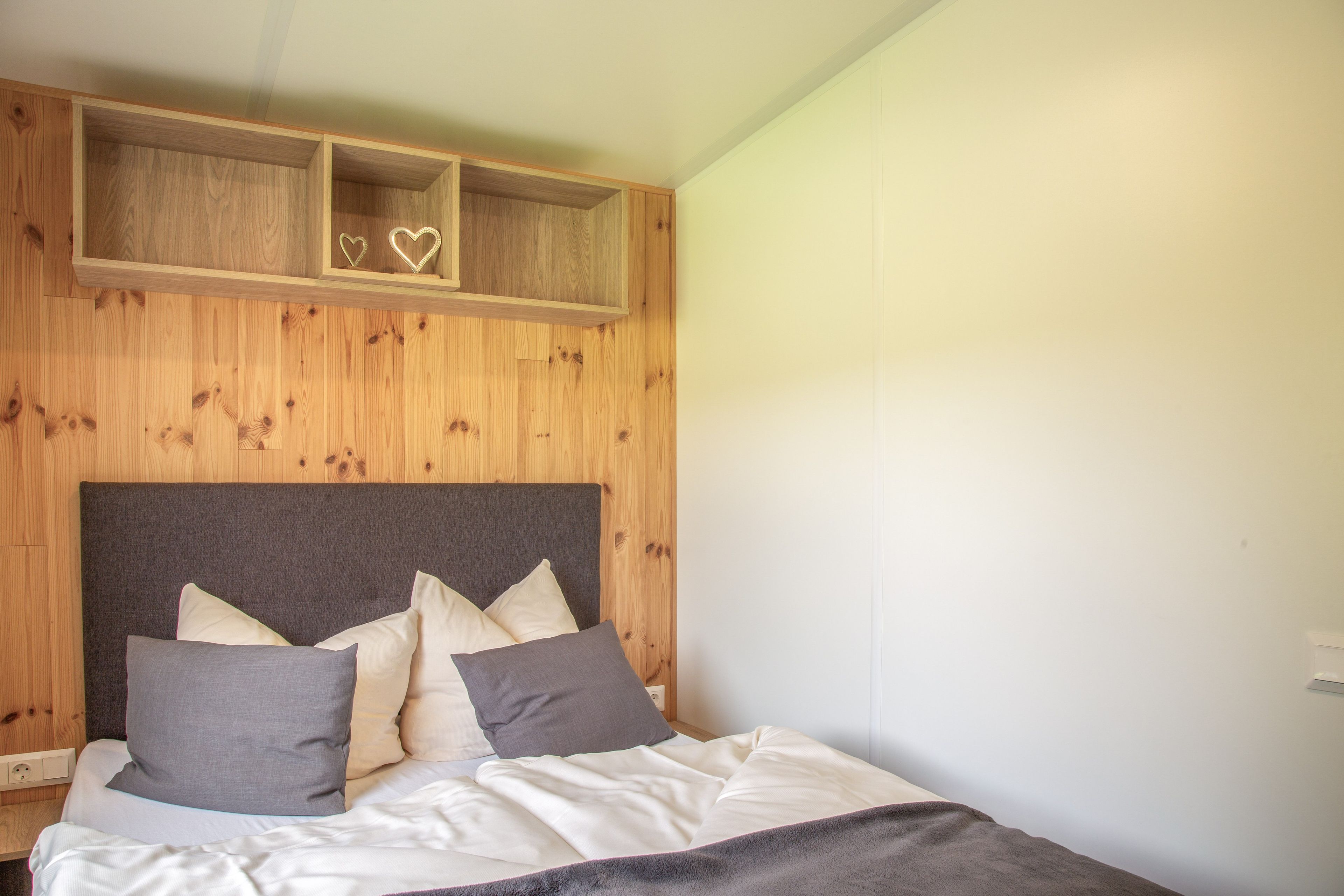 Ein Schlafzimmer mit einem Holzkopfende, einem Bett mit weißer und grauer Bettwäsche und zwei herzförmigen Dekorationen an der Wand.