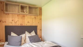 Ein Schlafzimmer mit einem Holzkopfende, einem Bett mit weißer und grauer Bettwäsche und zwei herzförmigen Dekorationen an der Wand.