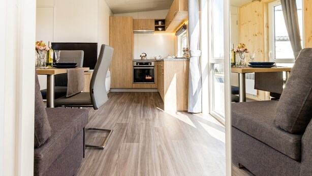A compact kitchen with wooden cabinets, a dining area with a table and chairs, and a sofa. - Tiny Home 'Laura' with Mountain Views, Wi-Fi, and Air Conditioning (Untergriesbach)