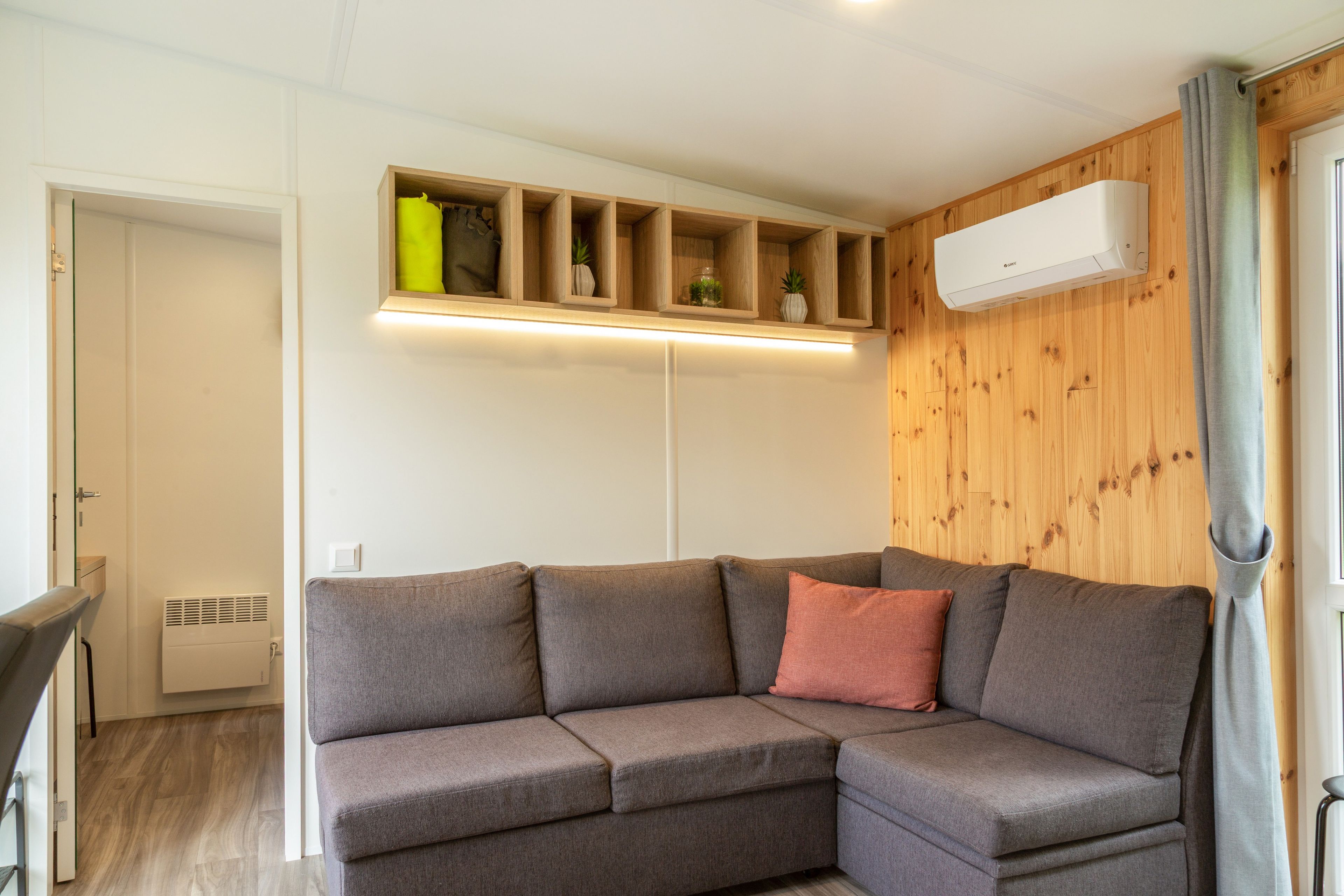 Ein modernes Wohnzimmer mit einer Eckcouch, eingebauten Regalen und einer Klimaanlage.