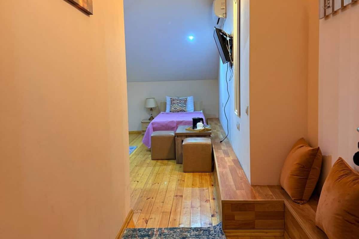 A narrow hallway leading to a bedroom with a bed, bedside table, and a mounted TV.