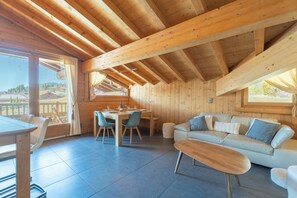 A wooden interior with a dining area, sofa, and large windows.