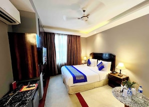 Una habitación de hotel con cama, televisor, escritorio, lámpara y ventilador de techo.